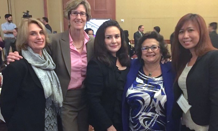 Sandra stands with four friends at a conference, the women have their arms around eachother and are wearing black blazers