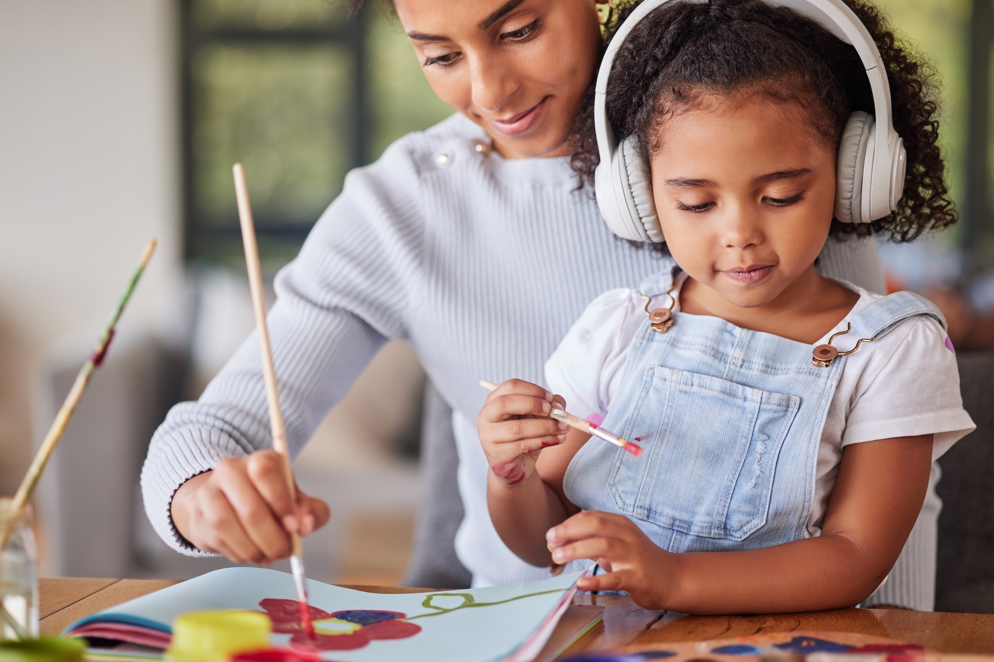 Child and parent paint together, child is wearing headphones